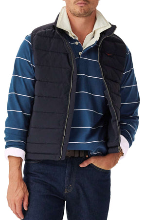 A man wears the RM Williams Albany Stripe Rugby under a navy quilted vest with dark jeans, hand in pocket, head partially cropped.