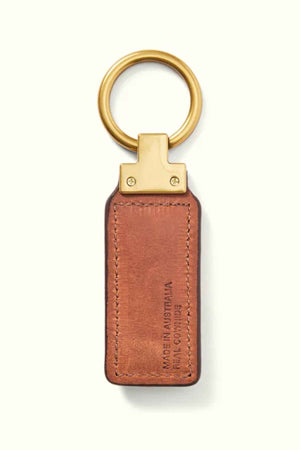 The RM Williams Angaston Key Fob is a brown full-grain leather keychain featuring antique brass hardware, complemented by a gold metal ring and attachment. The rectangular leather piece is embossed with "Made in Australia R.M.W. Comfort," maintaining a simple and elegant style throughout.