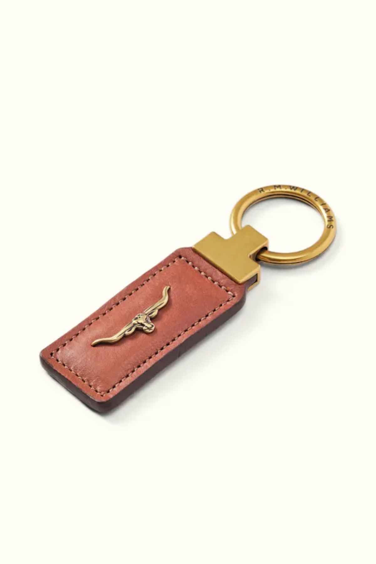 The RM Williams Angaston Key Fob showcases a metal bull emblem elegantly set on a rectangular piece of rich, full-grain leather. This sophisticated brown keychain is finished with an antique brass ring and gold-toned hardware. Made in Australia, it perfectly combines elegance and durability.