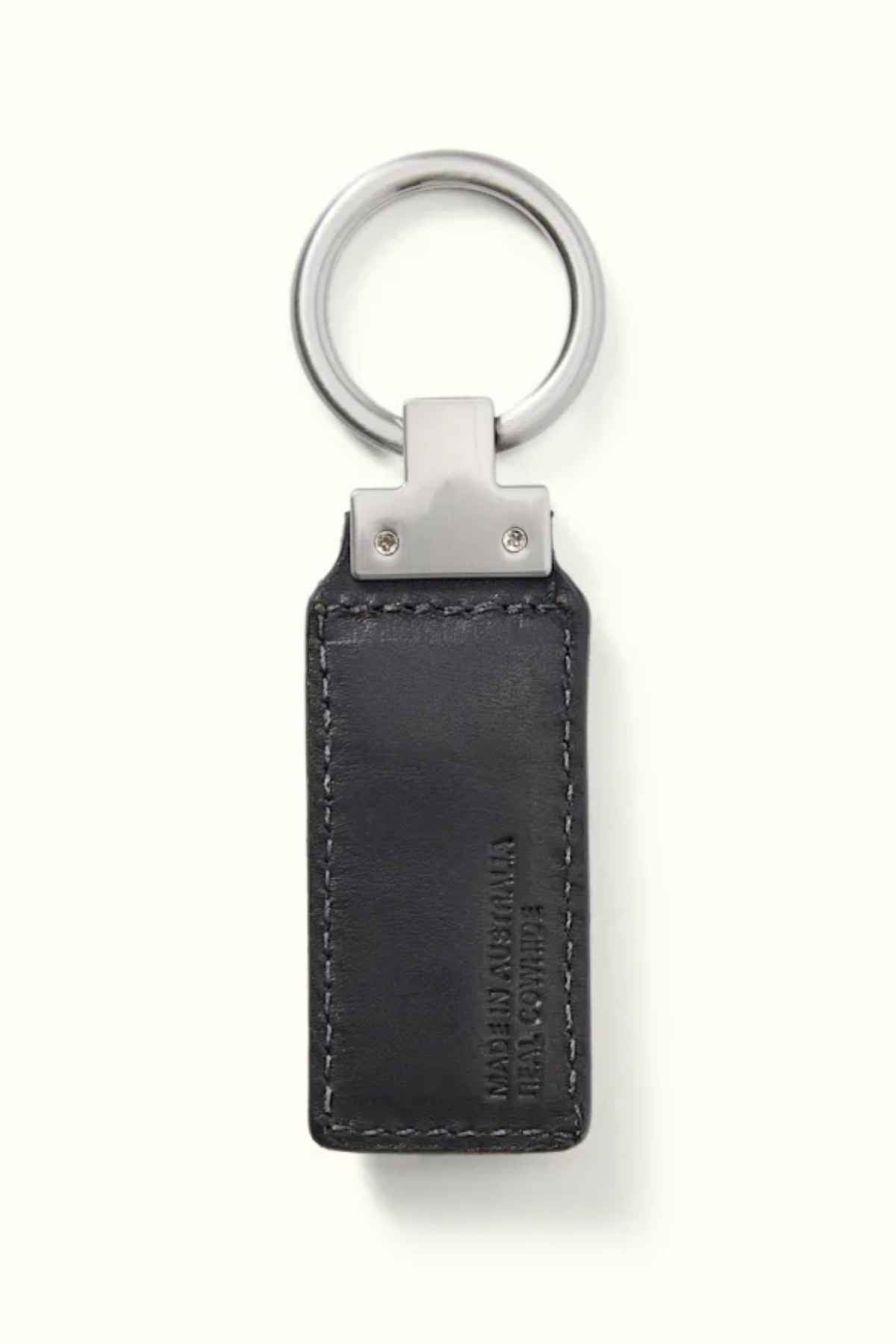 The RM Williams Angaston Key Fob is a rectangular black keychain made from full-grain leather, featuring visible stitching and a metal ring. The leather is embossed with text and includes a subtle longhorn logo, though the details aren't entirely clear. It is elegantly set against a light, plain background.