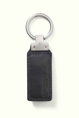 The RM Williams Angaston Key Fob is a rectangular black keychain made from full-grain leather, featuring visible stitching and a metal ring. The leather is embossed with text and includes a subtle longhorn logo, though the details aren't entirely clear. It is elegantly set against a light, plain background.