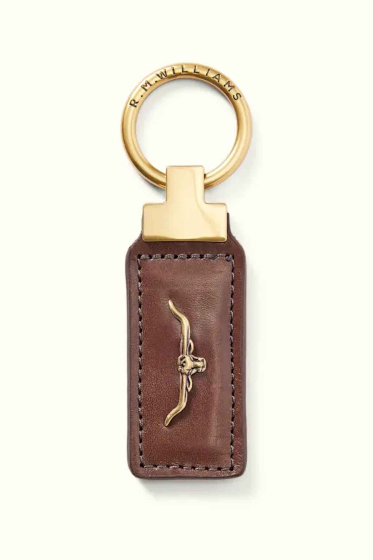 The RM Williams Angaston Key Fob is a brown leather keychain made from full-grain leather with gold accents and features a metal bull's head emblem. The circular keyring is inscribed with text and decorated with antique brass hardware, adding timeless elegance.