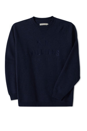 The RM Williams Bale Sweatshirt is a navy blue fleece, featuring "R.M. Williams EST. 1932" embossed on the front in a darker shade. Made from an organic cotton blend, it embodies outback style with a visible brand tag at the neckline and is showcased flat against a white background.