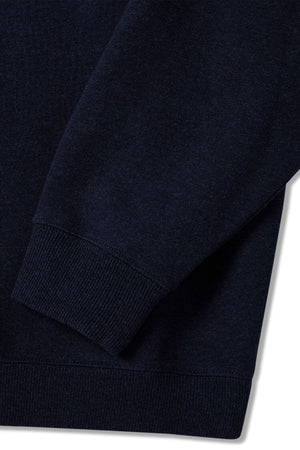 Close-up of the RM Williams Bale Sweatshirt sleeve and torso, featuring a dark blue fleece crafted from an organic cotton blend. The fabric has a slightly textured look, complemented by ribbed cuffs and hem. The white background highlights this outback-style garment's rich color and texture.