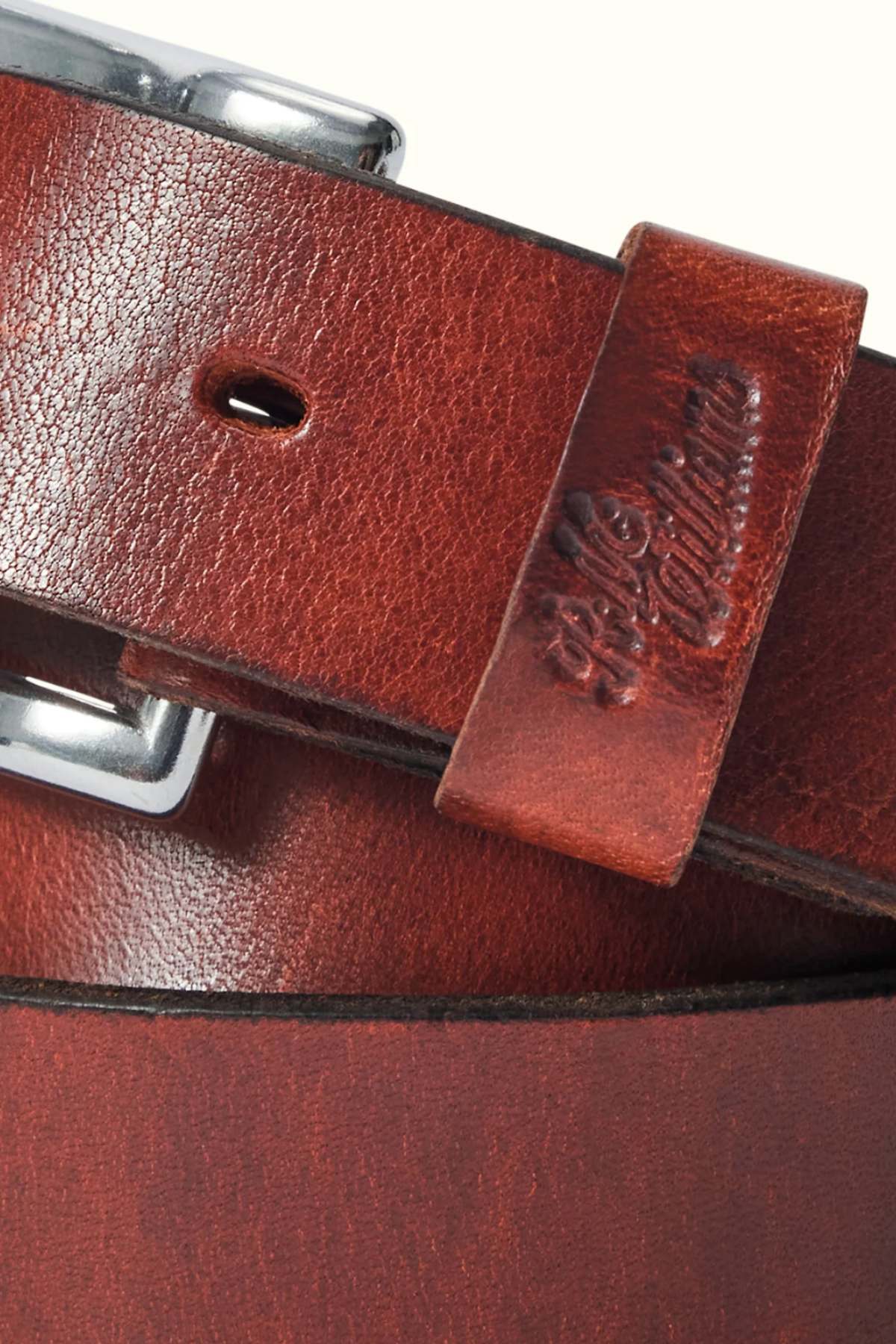 Close-up of the RM Williams Berwick Belt, featuring brown textured leather with a roller-style buckle and an embossed longhorn emblem on the leather keeper. The belt has a slightly worn finish for added character.