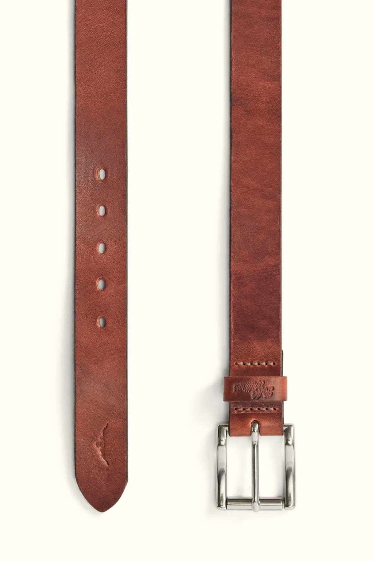 The RM Williams Berwick Belt is shown laid flat, featuring brown leather, a silver roller buckle, punched holes and pointed tip on one end, with embossed branding near the leather keeper on the other.
