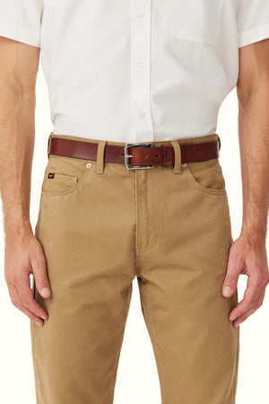 A person is shown from shoulders to mid-thigh wearing a white short-sleeve button-up shirt, tan pants, and the RM Williams Berwick Beltโa brown leather belt with a roller-style buckle.