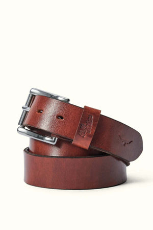The RM Williams Berwick Belt is a coiled brown leather belt with a roller-style silver buckle, embossed logo, and sturdy keeper, displayed on a light background.