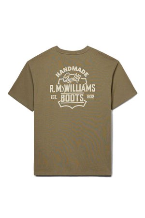 The RM Williams Boot T-Shirt is a khaki short-sleeve tee featuring a bold, vintage-style white graphic on the back that reads "Handmade Quality R.M. Williams Boots Est. 1932.