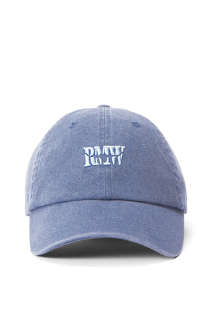 Front view of the RM Williams Branded Twill Cap in light blue organic cotton with white "PAUW" embroidery in a bold, playful font. Features include an adjustable strap, curved brim, and ventilation eyelets for comfort.