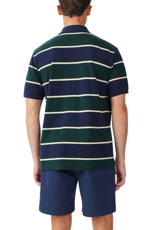 A man stands facing away, wearing the RM Williams Bright Polo in navy and green stripes with white lines, crafted from organic cotton, paired with dark blue shorts.