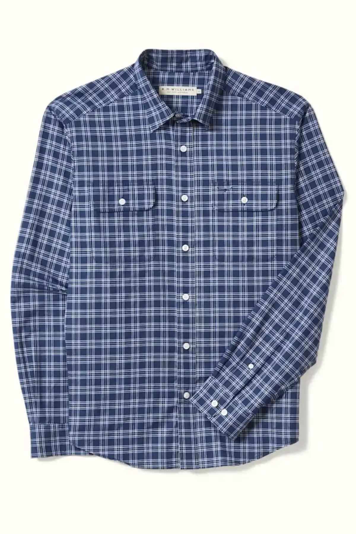 The RM Williams Classic Shirt is a long-sleeve, regular fit shirt featuring a blue and white plaid pattern. Made from organic cotton, it includes two chest pockets with buttoned flaps and white buttons down the front and on the cuffs. The lightweight fabric makes it ideal for smart casual wear.