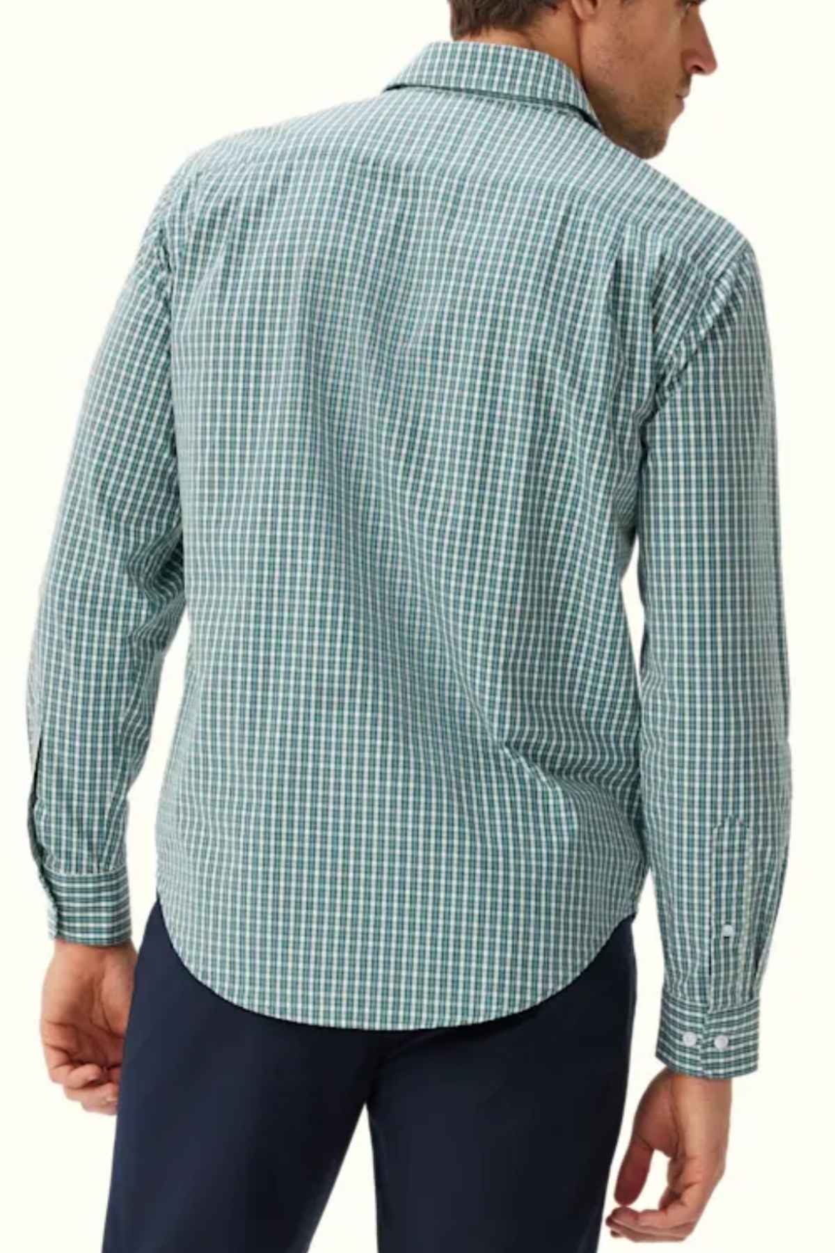 A man is seen from the back wearing an RM Williams Classic Shirt in green and white gingham check, made of cotton poplin. He is also dressed in dark blue pants and is standing against a plain light background, with his head turned slightly to the side.