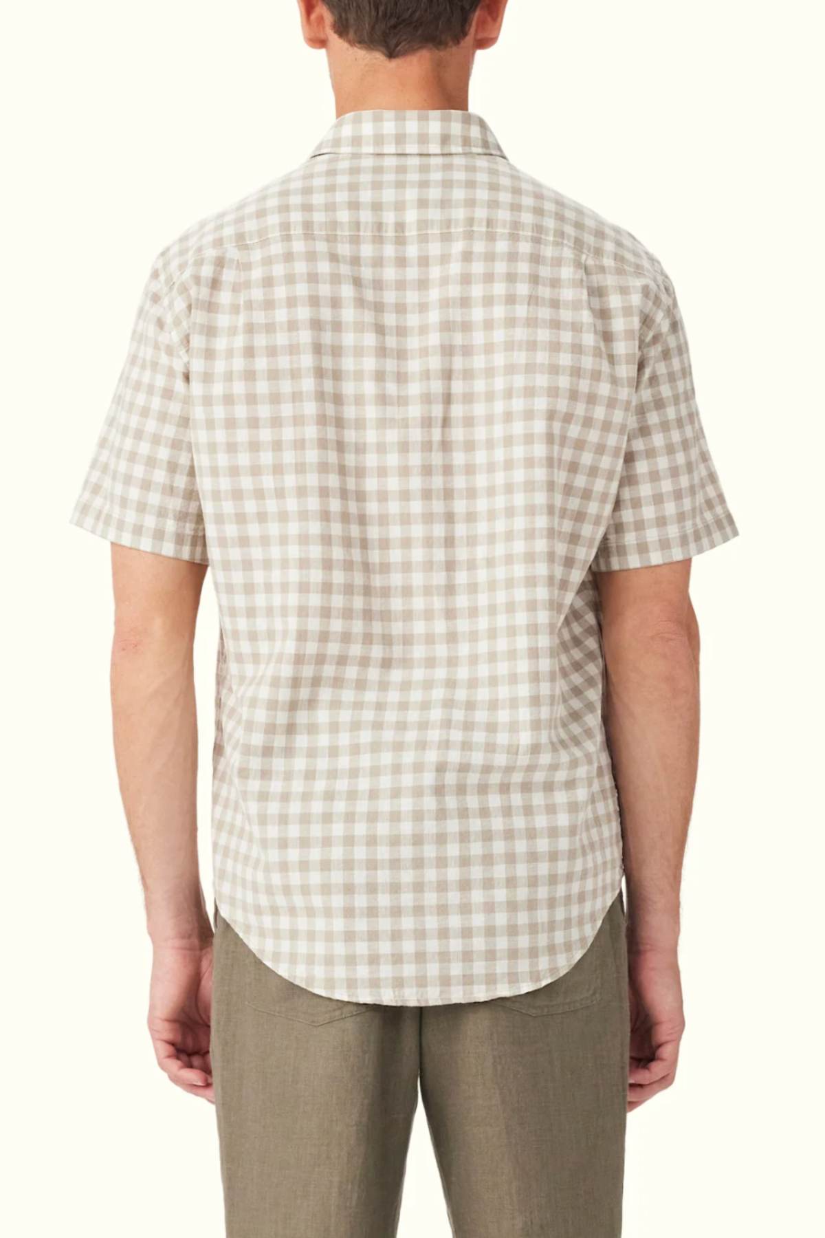 A man sporting the RM Williams Classic Short Sleeve Shirt in beige and white gingham, seen from behind, showcases timeless style. Paired with light brown pants, this outfit stands out against a simple, light backdrop.