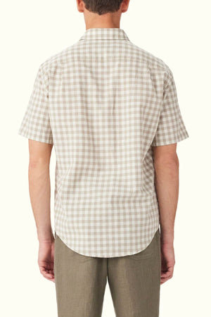 A man sporting the RM Williams Classic Short Sleeve Shirt in beige and white gingham, seen from behind, showcases timeless style. Paired with light brown pants, this outfit stands out against a simple, light backdrop.
