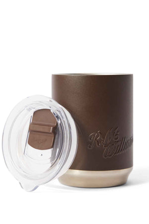 The RM Williams Coffee Cup is a brown travel mug with a transparent lid and folding brown tab. It features a metallic silver base and embossed "R.M. Williams" text on the side, offering style and sustainability for your coffee routine.