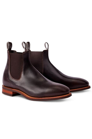 A pair of dark brown RM Williams Comfort Craftsman leather boots with a polished finish. The boots feature elastic side panels, pull tabs at the back and front, and brown wooden soles with a slight heel. Made in Australia, these sleek and elegant Chelsea boots highlight superior craftsmanship.