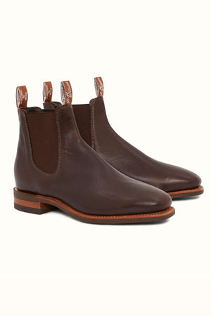 The RM Williams Comfort Kangaroo Craftsman Boot is a pair of brown Chelsea boots crafted from premium Kangaroo leather, featuring elastic side panels and pull tabs. The sleek design includes a polished leather finish, logo text on the pull tabs, a low stacked heel, and a stitched sole. Made in Australia, these boots are positioned together on a plain background.