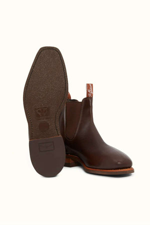 A pair of RM Williams Comfort Kangaroo Craftsman Boots, made from brown Kangaroo leather in Australia, are shown against a plain background. One boot stands upright, highlighting its side profile and elastic gusset, while the other is tilted to display the textured sole and heel. Both boots feature a pull tab at the back.