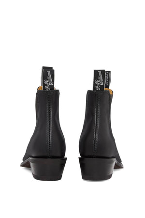 Back view of the RM Williams Comfort Lady Yearling Rubber Sole Boot in black leather, displaying text on the pull tabs. These elegant Chelsea boots are made from Yearling leather, featuring elastic sides, a small block heel, and visible stitching.