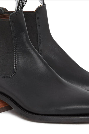 A close-up of the RM Williams Comfort Lady Yearling Rubber Sole Boot showcases its sleek black Chelsea design, featuring elastic side panels, a low block heel, and the smooth texture of Yearling leather for a minimalistic look.