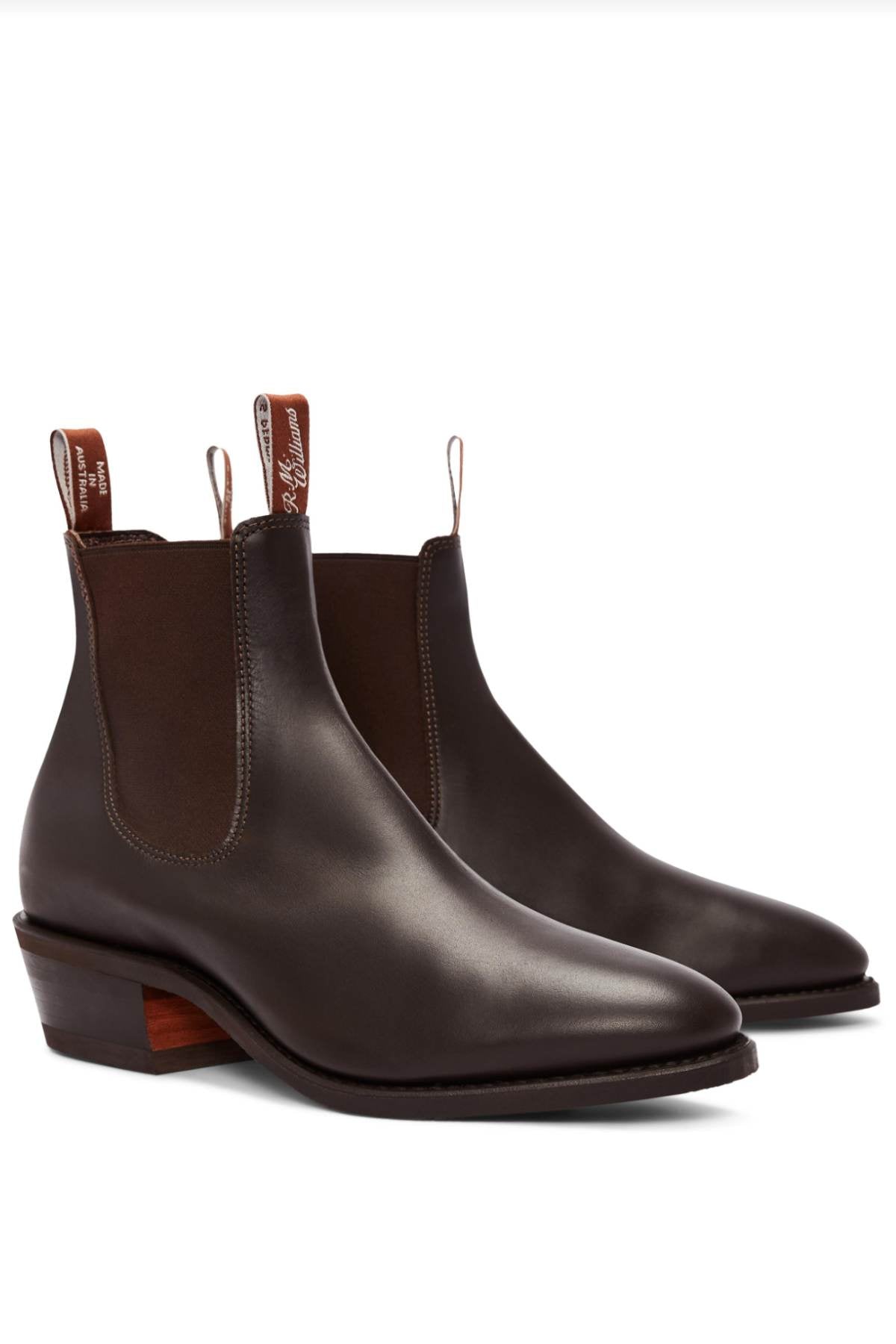 The RM Williams Comfort Lady Yearling Rubber Sole Boot is a pair of dark brown leather Chelsea boots with elastic side panels and pull tabs, featuring a block heel and a smooth finish.