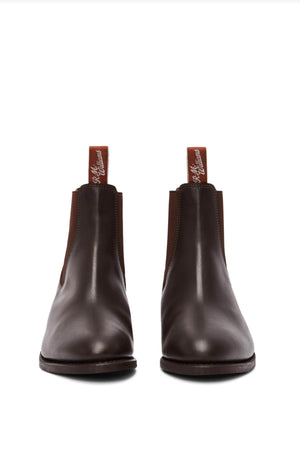 The RM Williams Comfort Lady Yearling Rubber Sole Boot, a pair of dark brown leather Chelsea boots with elastic side panels and pull tabs at the back, featuring a subtle block heel, is placed on a white background.