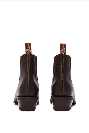 The RM Williams Comfort Lady Yearling Rubber Sole Boots are pictured from the back, featuring dark brown leather in the classic Yearling boot style. The boots have reddish-brown pull tabs with white cursive text and exhibit a slight heel along with visible stitching, elegantly displayed against a plain white background.