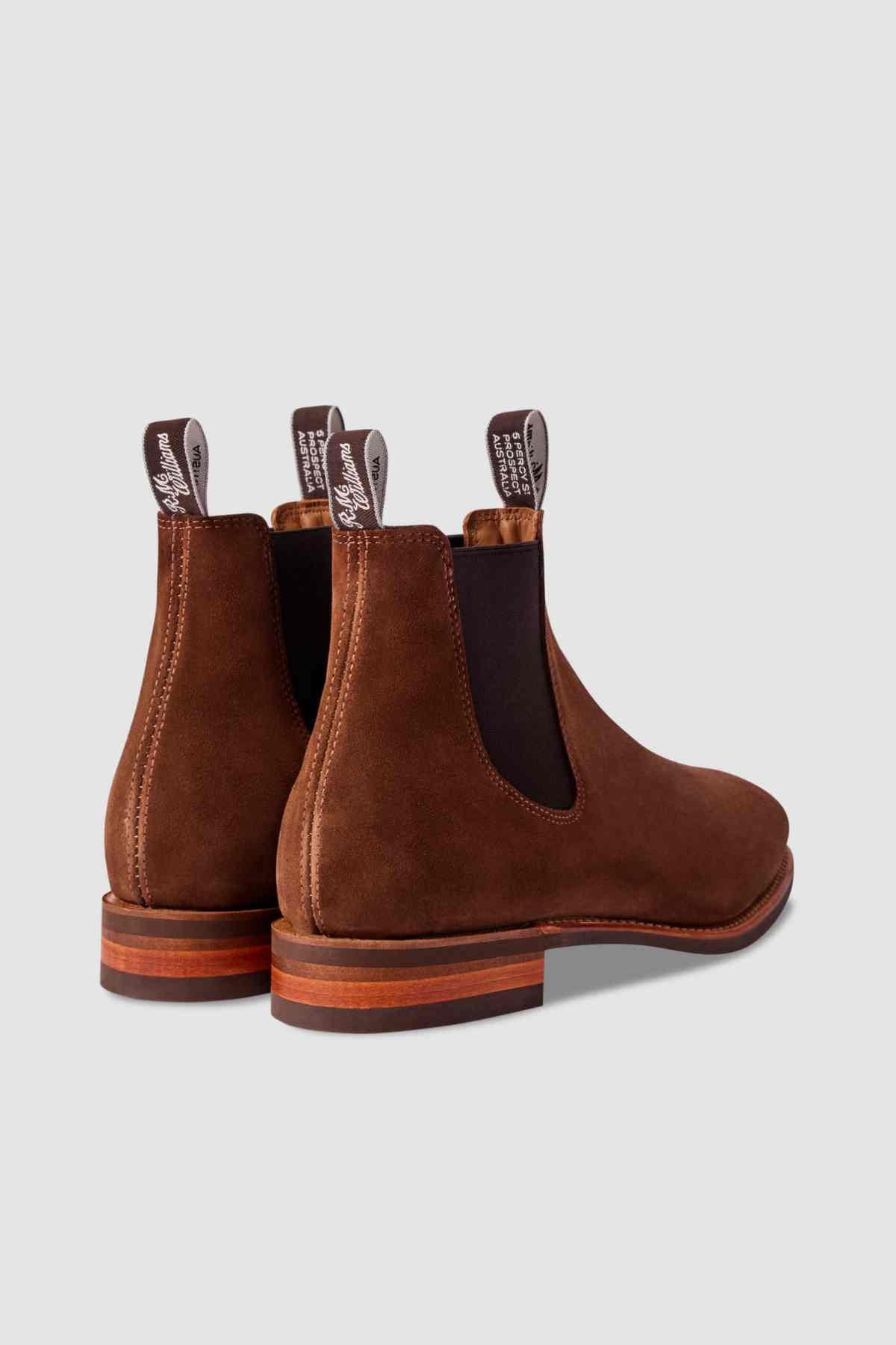 The RM Williams Comfort Suede Craftsman Boot, a brown suede Chelsea boot with dark elastic side panels and pull tabs, is shown from the back and side on a plain light gray background. Made in Australia for lasting style and comfort.