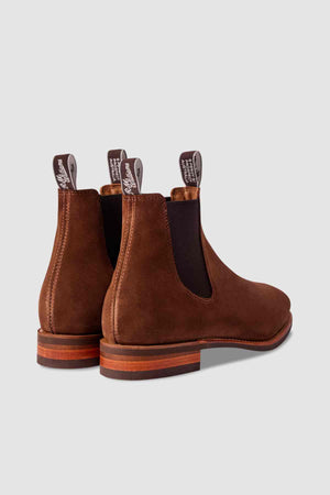 The RM Williams Comfort Suede Craftsman Boot, a brown suede Chelsea boot with dark elastic side panels and pull tabs, is shown from the back and side on a plain light gray background. Made in Australia for lasting style and comfort.