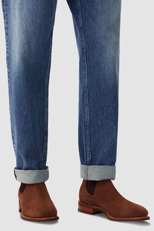 A person wearing cuffed blue jeans and the RM Williams Comfort Suede Craftsman Boot, made in Australia, stands on a light gray background.