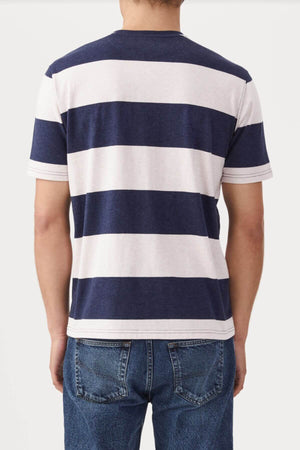 Rear view of a person in a RM Williams Copley T-Shirt, featuring navy and white broad horizontal stripes, short sleeves, and classic striped style. They are wearing blue jeans against a plain white background.