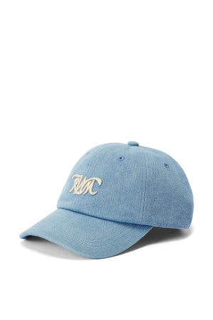 The RM Williams Cursive Twill Cap is a light blue denim baseball cap made from organic cotton, with a curved brim and white embroidered script initials on the front.