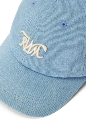 The RM Williams Cursive Twill Cap is a light blue organic cotton cap with a curved brim, white embroidered "RMC" text on the front, visible stitching, and two crown ventilation eyelets.