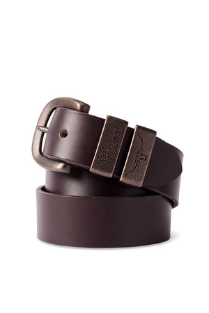 The RM Williams Drover Belt, crafted from vegetable-tanned leather, showcases a rolled-up dark brown design complete with an antique brass buckle and an engraved metal tip. Its smooth texture enhances its sophisticated appeal.