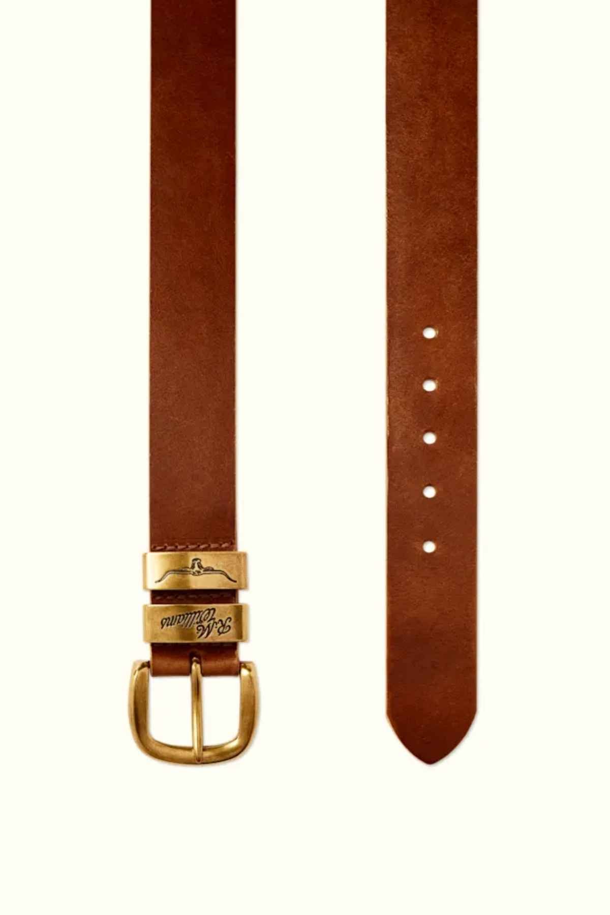 The RM Williams Drover Belt, made in Australia from brown pull-up leather, features a gold-toned buckle with an engraved logo. The belt showcases multiple adjustment holes and tapers to a point at one end, displaying timeless elegance when shown vertically.