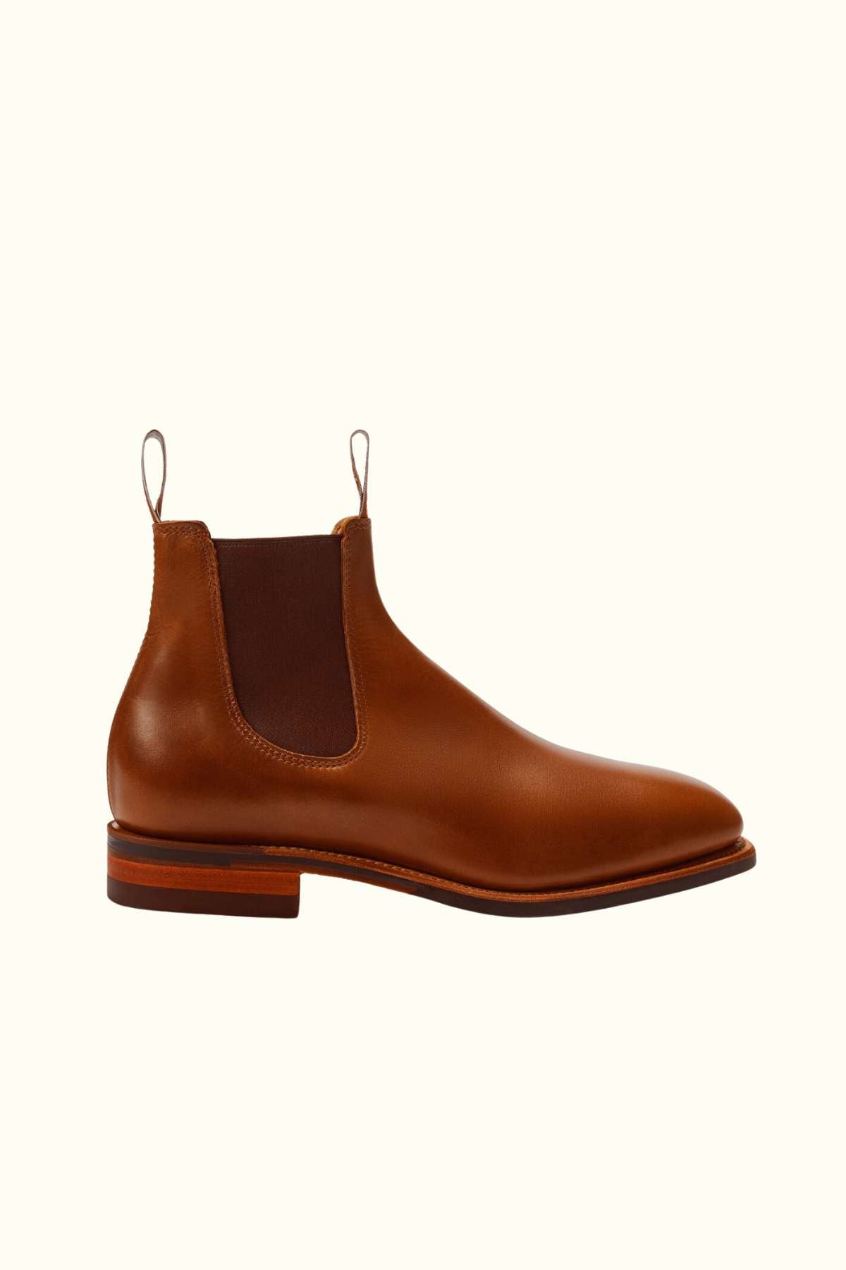 The RM Williams Dynamic Flex Craftsman Boot is a brown yearling leather Chelsea boot featuring elastic side panels, front and back pull tabs, and a low stacked wooden heel, shown on a plain light background.