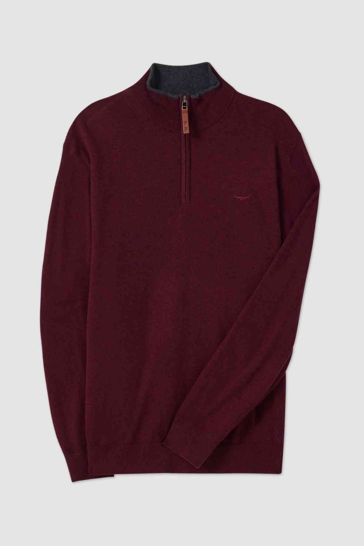 The RM Williams Ernest Sweater is a fine gauge merino sweater in burgundy with a dark gray inner collar. This quarter zip sweater features a small embroidered logo on the left chest and a leather pull tab on the zipper. The fabric appears to be soft and of medium thickness, laid flat against a light gray background.