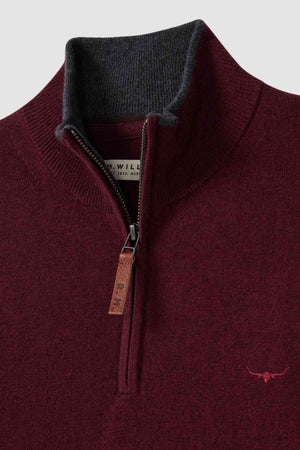 A close-up of the RM Williams Ernest Sweater, showcasing its maroon quarter-zip design with a brown leather pull tab on the zipper. This fine gauge Merino wool sweater features a ribbed high collar with dark gray lining and a small embroidered red logo on the left chest. The label inside the collar is partially visible.