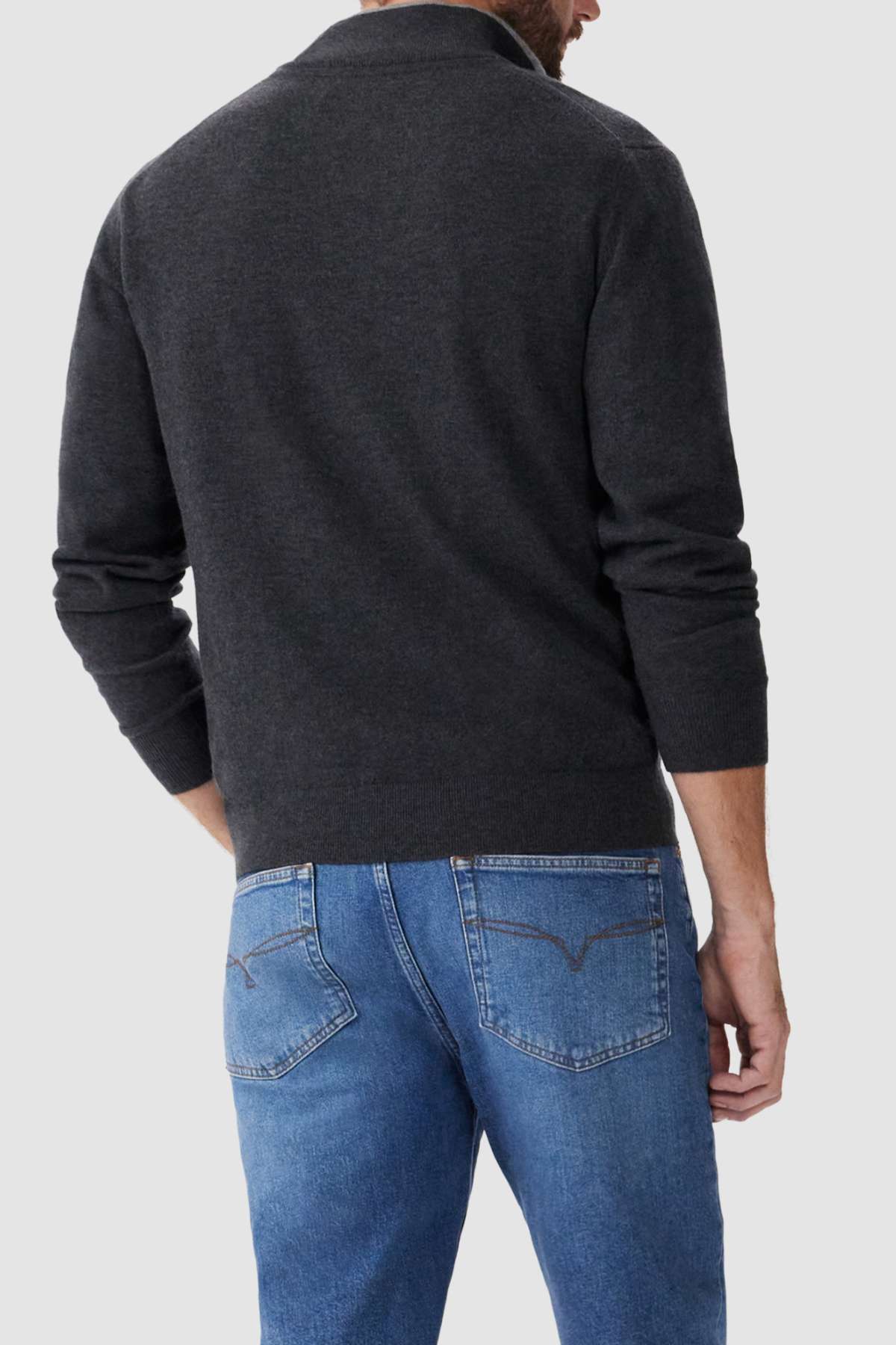 A man is seen from the back wearing a dark gray RM Williams Ernest Sweater made of fine gauge merino wool and blue jeans. The sweater has a plain design, and the jeans feature classic stitching on the back pockets. The background is a solid light gray.
