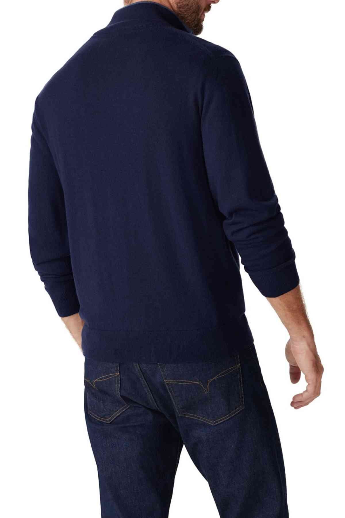 A man wearing the RM Williams Ernest Sweater in dark blue and matching jeans stands with his back to the camera, glancing slightly to the side.