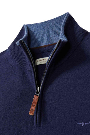 Close-up of the RM Williams Ernest Sweater in navy blue fine gauge merino, featuring a brown leather zipper pull, blue inner collar lining, small chest logo, and an inner label reading "R.M. Williams Est. 1932.