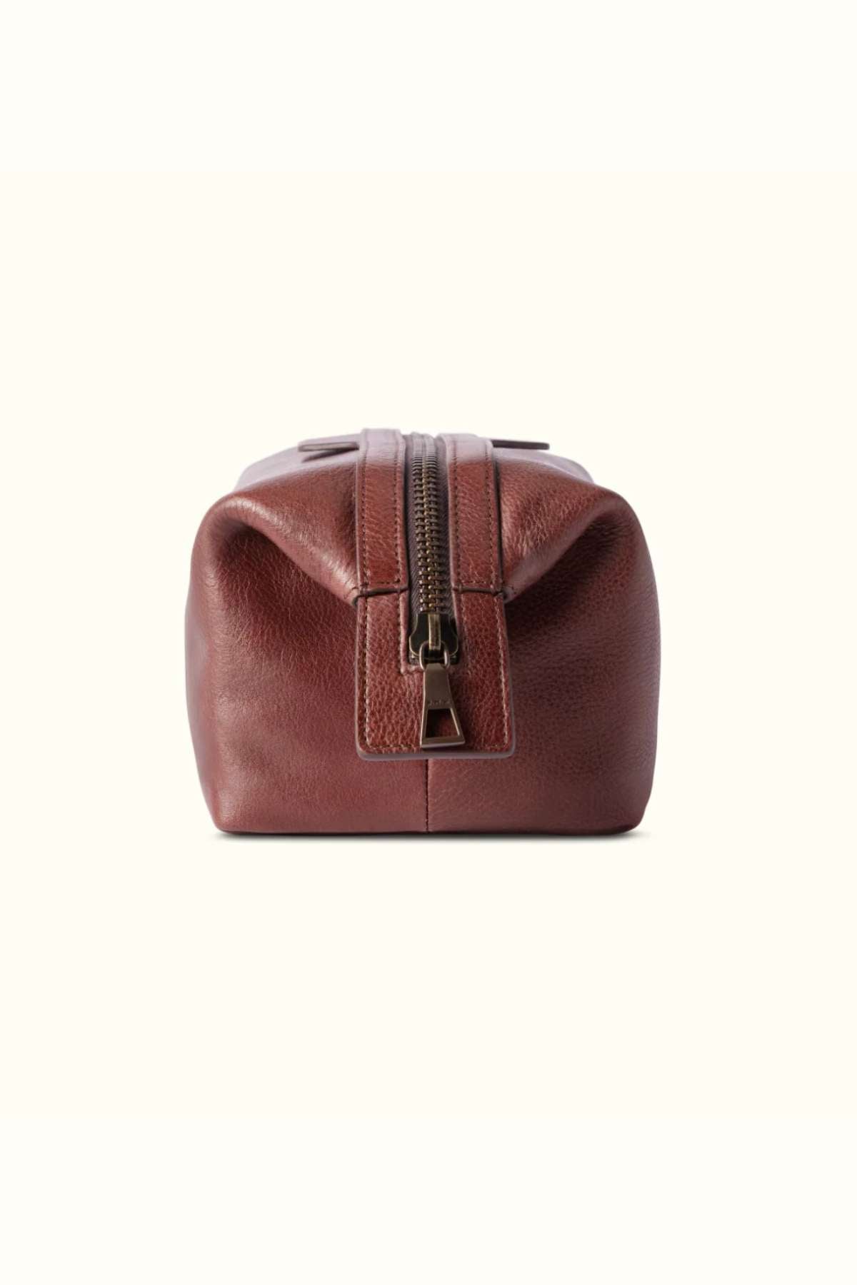 The RM Williams Farrier Washbag is a brown leather washbag crafted from tumbled grain leather with a textured surface and central zipper. Its simple, rectangular design is elegantly showcased against a plain, light background.