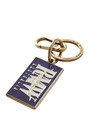The RM Williams Heritage Logo Enamel Key Ring is a rectangular metal key ring with a purple background and raised white "ARMY" and "AUSTRALIA" lettering, attached to a bronze-colored brass keyring.