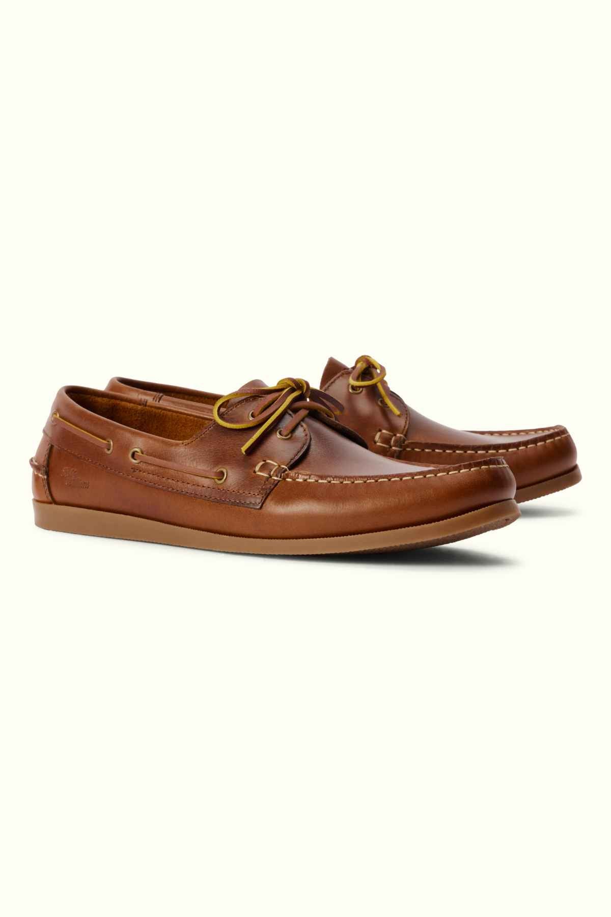 A pair of RM Williams Islet Moccasin shoes in brown leather with laces, featuring stitching details on the toe and sides, placed against a plain light background. The shoes have a low heel and a moccasin-style design.