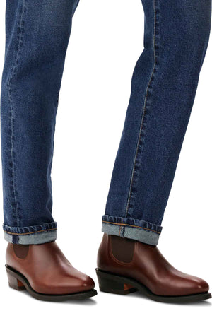 A person in rolled-up blue jeans and the RM Williams Comfort Lady Yearling Boot is walking. These boots, crafted from Spanish pull-up leather with elastic side panels, are skillfully handmade in Australia and feature a low heel.