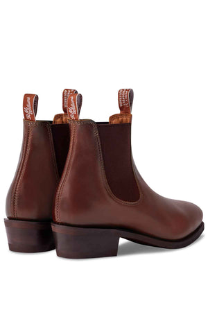 Handmade in Australia, the women's RM Williams Comfort Lady Yearling Rubber Sole Boot features elastic side panels and heel pull-tabs with white text. Made from Spanish brown leather, these Chelsea boots showcase a low stacked heel and are shown from the back and slightly to the side.