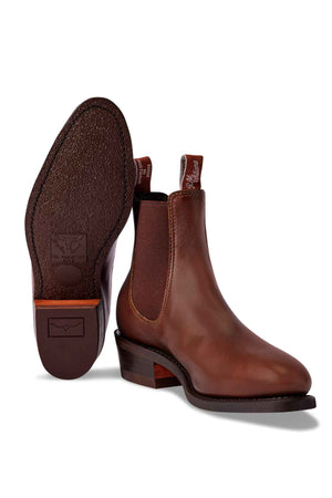 The RM Williams Comfort Lady Yearling Rubber Sole Boot, handmade in Australia, is a pair of women's Chelsea boots made from Spanish pull-up leather with elastic side panels and pull tabs. One boot stands upright while the other lies on its side, showing a textured sole and low heel.