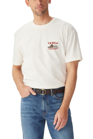 A man wears the RM Williams Last T-Shirt in white with red chest text and graphics, paired with blue jeans and a black textured belt. For the perfect fit, consult our size guide or contact customer service for chest measurement help.