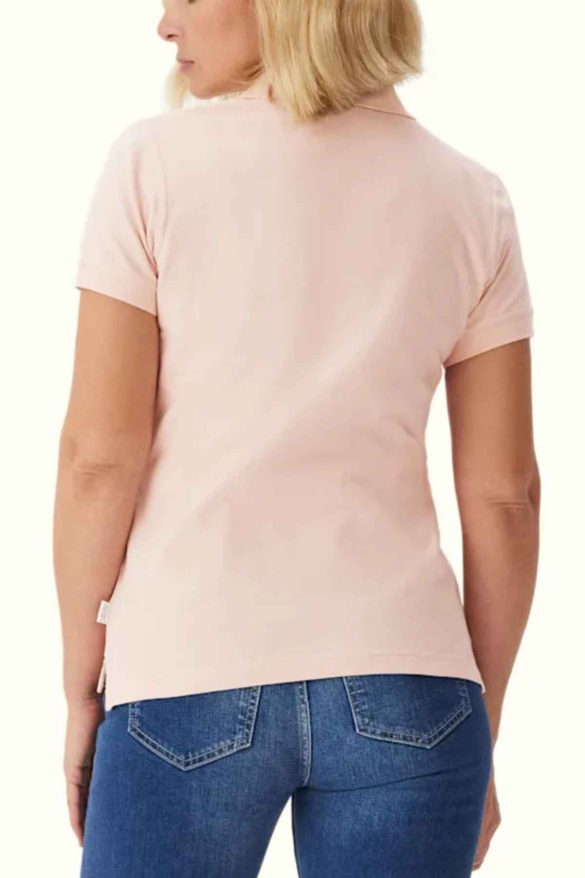 A person with blonde hair is seen from the back, wearing an RM Williams Margaret Polo in light pink pique cotton with a ribbed collar and short sleeves, paired with blue jeans.